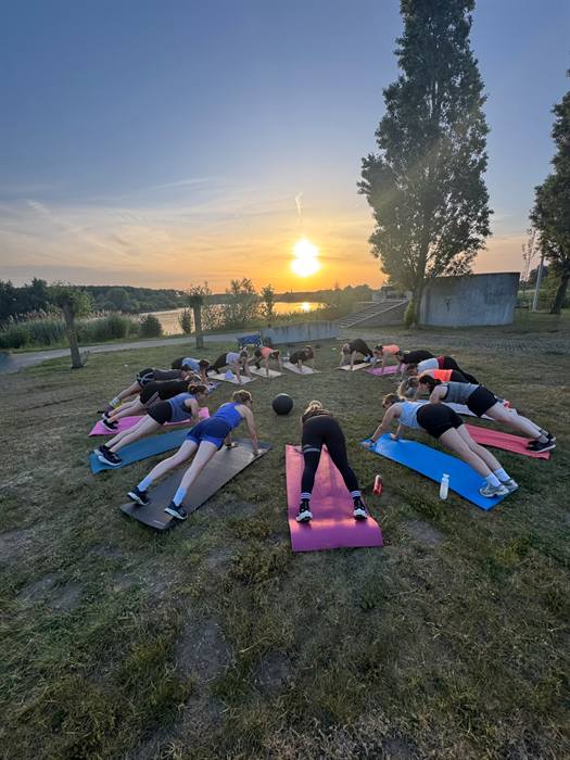 Groep vrouwen in plankhouding in een kring aan het water bij zonsondergang