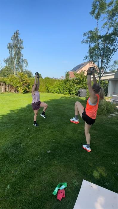 Twee vrouwen tillen gewichten boven het hoofd in een tuin